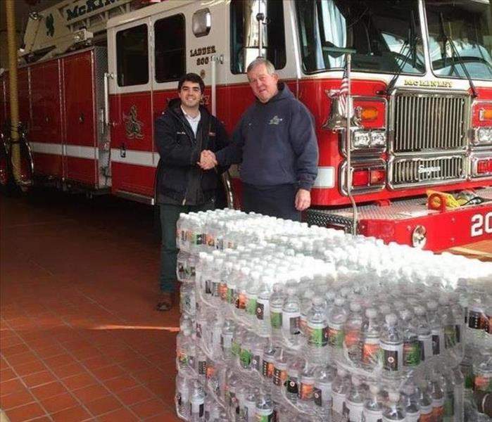 Crew member shaking hands with local Fire Chief while donating SERVPRO water bottles.